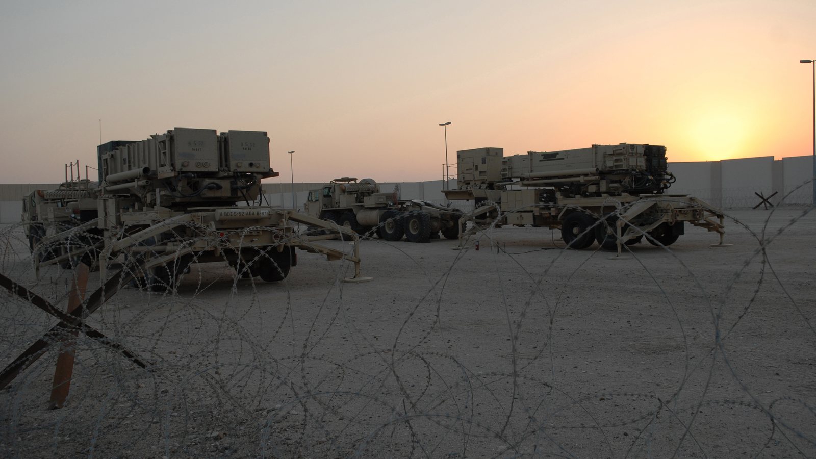 Patriot PAC-2 and PAC-3 missile launchers at an air base at sunset, behind razor wire
